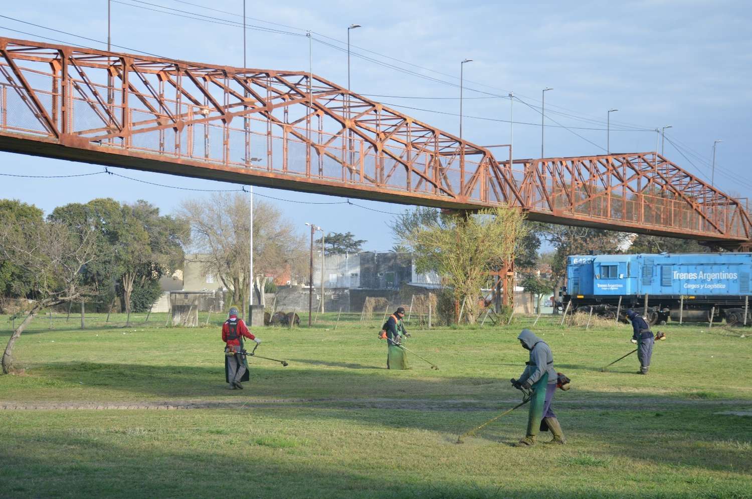 En la zona del ferrocarril, bajo el puente peatonal, los trabajadores proceden al corte de césped.